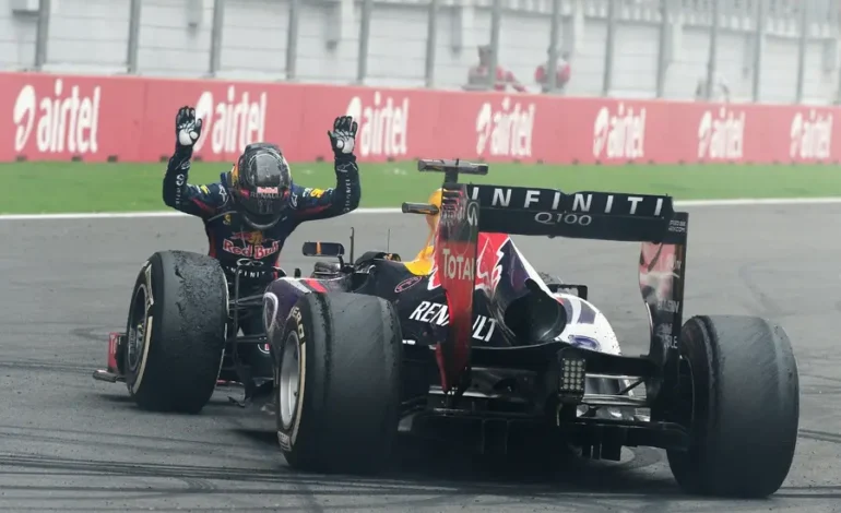 A high-speed Formula 1 car racing on the Buddh Circuit track at sunset, featuring a digital overhead sign that reads "F1 RETURNS TO INDIA?" and a packed grandstand with fans waving Indian flags.